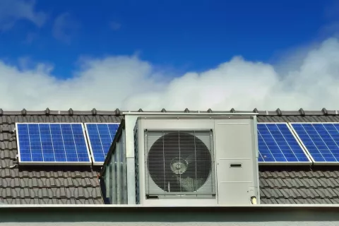 Im Vordergrund steht eine Wärmepumpe und im Hintergrund ist eine Photovoltaikanlage auf dem Dach zu sehen.